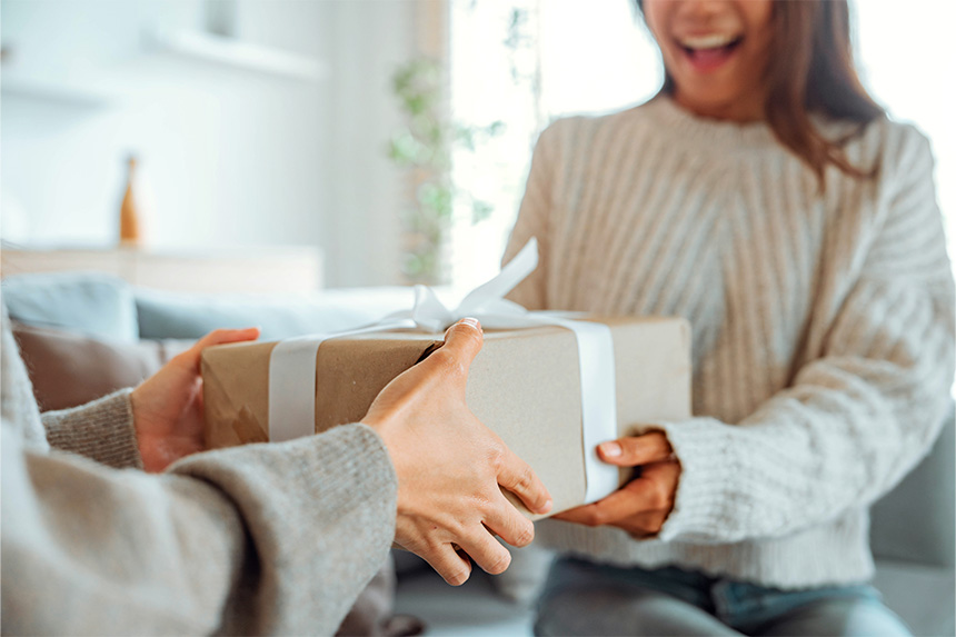 A young couple in neutral sweaters exchange gifts.