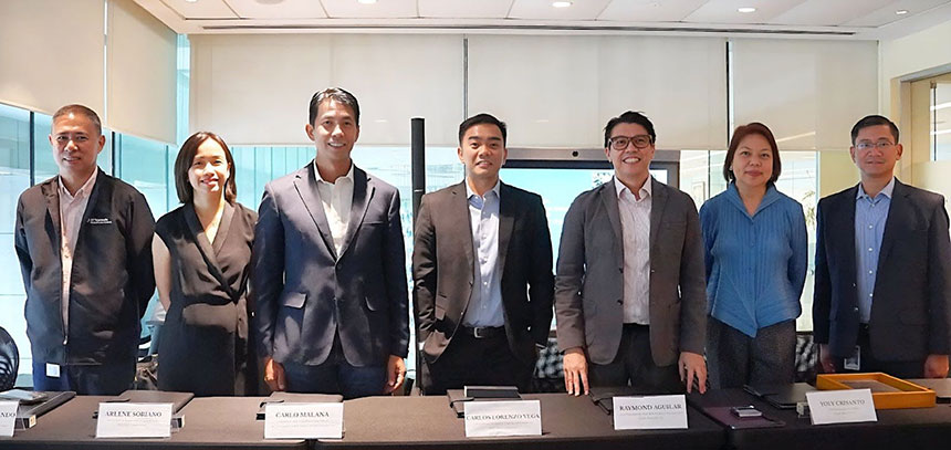 A group of seven people in business attire standing behind a table with nameplates in a conference room.