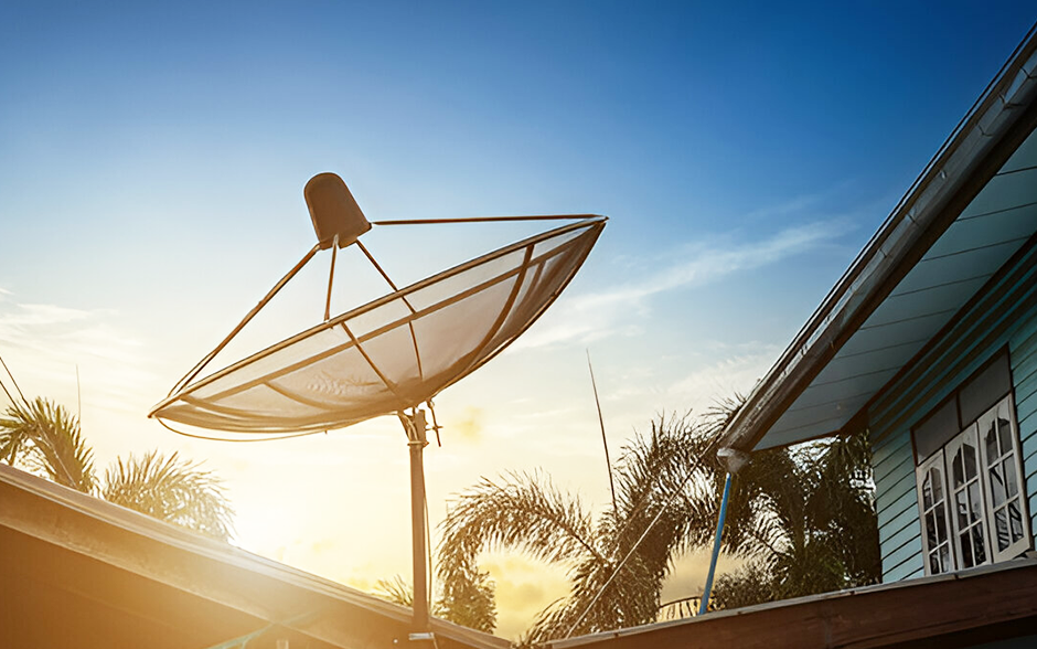 A black satellite dish on the roof of a country house, with a dramatic sunset sky and blue sky in the background.