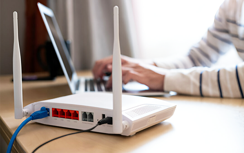 A focus shot of an internet router on a working table, with a blurred man in the background.