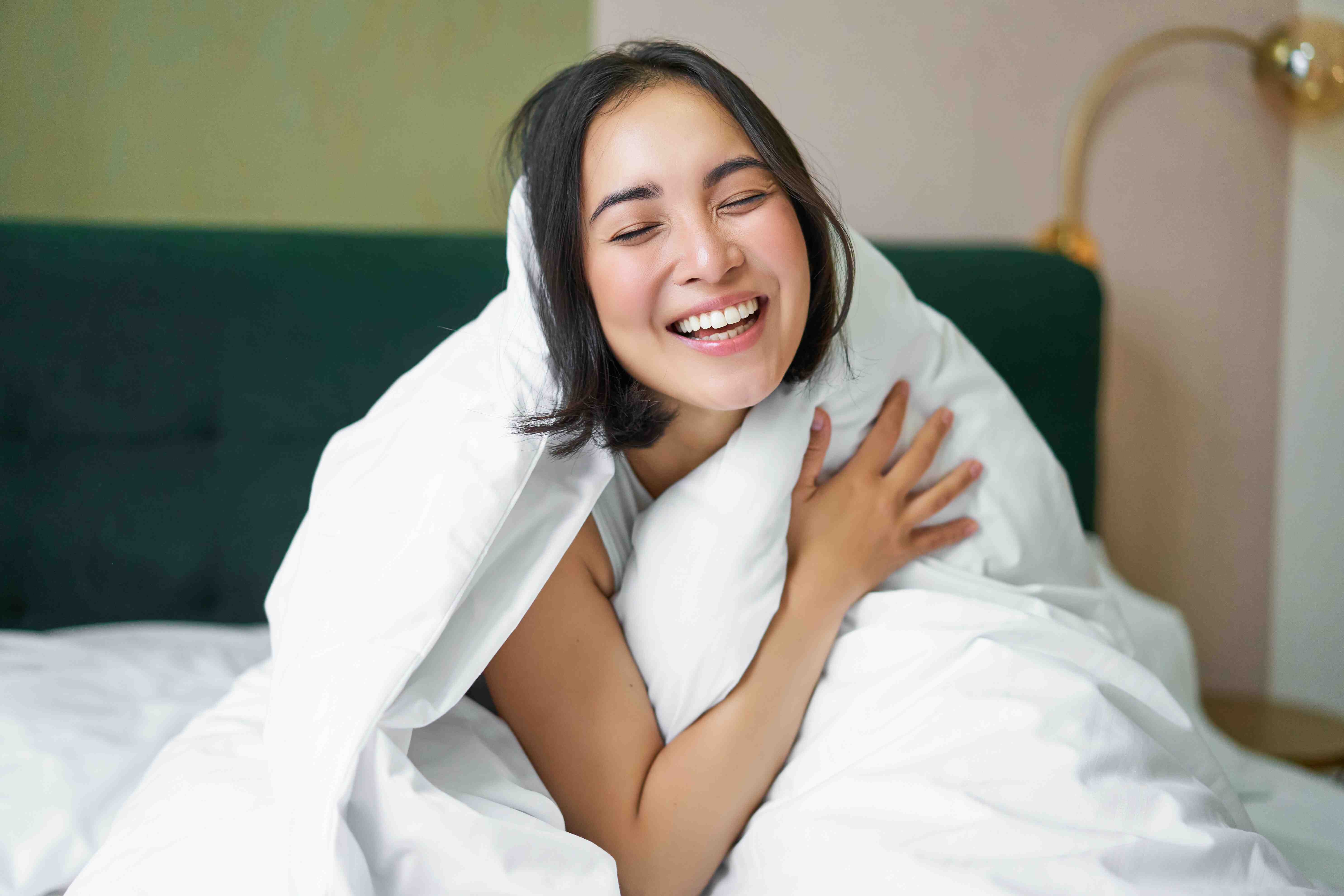 A smiling woman wrapped in a white blanket.