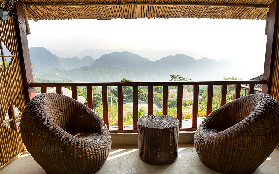 Modern rattan armchairs on the terrace with a fence and bamboo roofing with a rural view.