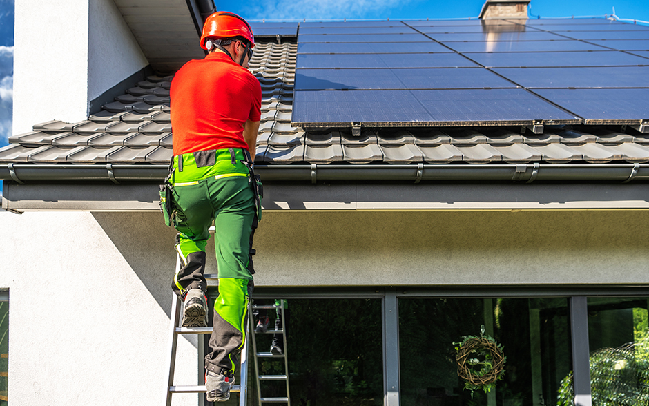 Professional worker in safety gear installing solar panels on a roof.