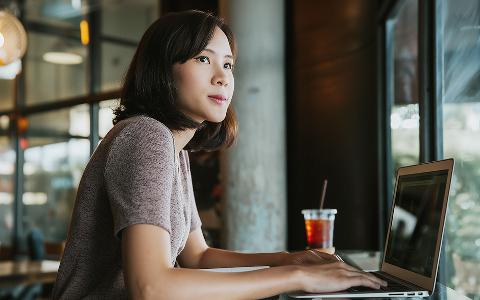 Asian woman sitting in a cafe with iced tea trying to compute her ITR.
