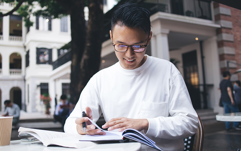 Asian man sitting outdoors with notebook and pen trying to understand ITR for self-employed individuals.