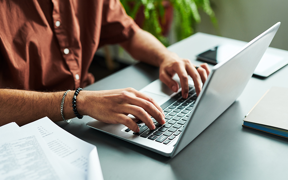 Closeup of Asian man sitting and typing on the computer googling ITR requirements.