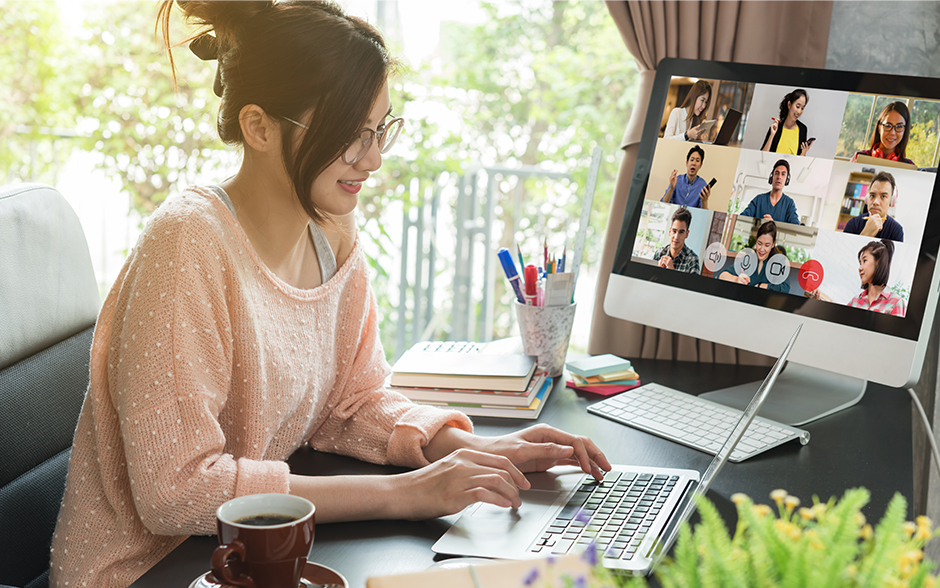 A young Asian woman on a video call with her colleagues while working on her laptop at home.