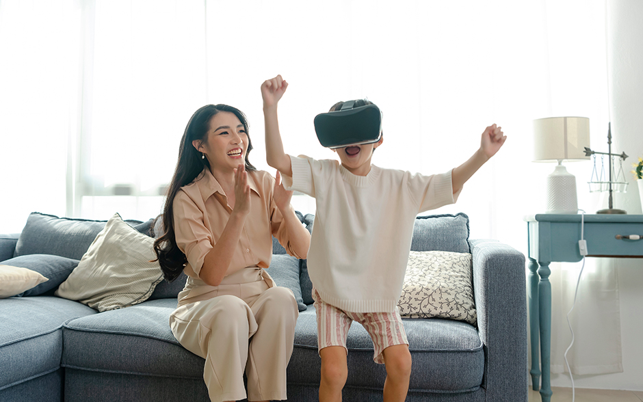 Young Asian mom smiling at her son playing a game using a virtual reality headset.