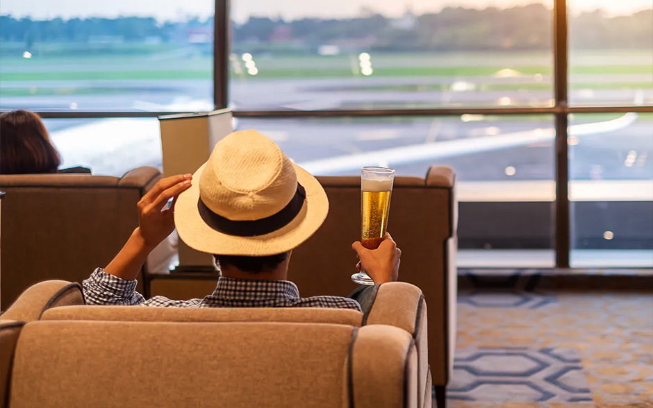 Asian man relaxing and drinking beer in an airport loungeâone of the Globe Platinum perks.