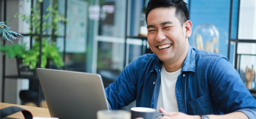 Asian male laughs while working on his laptop.