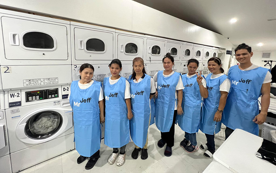 The staff of a Mr. Jeff branch pose for a photo at a laundromat wearing their blue apron uniforms.