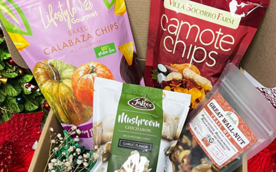 A holiday gift box filled with Apotheca Integrative Pharmacy's locally made healthy snacks, including calabaza chips, camote chips, mushroom crackers, and nut mix.