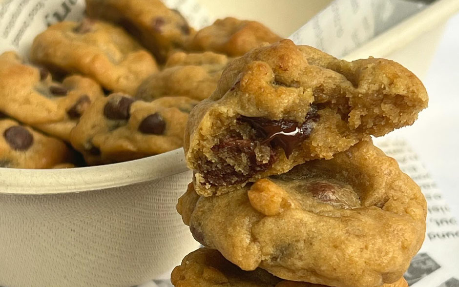 Locally made Chewychips Cookies with gooey chocolate centers, placed on parchment-style paper with more cookies in a bowl behind.