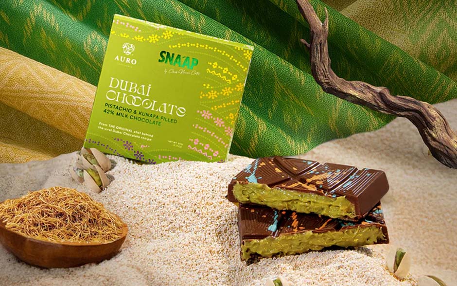 Auro Chocolate is displayed on sand with a green woven background.