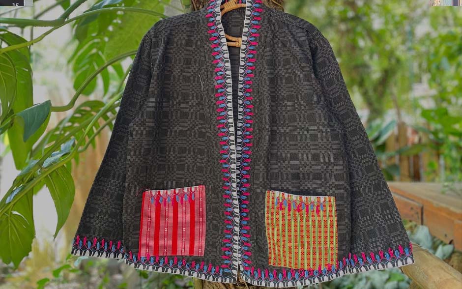 A handwoven jacket with colorful embroidered pockets and detailing, hanging on a tree branch.