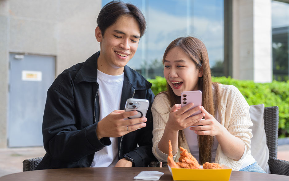 Two co-workers watching something on their smartphones while having lunch.