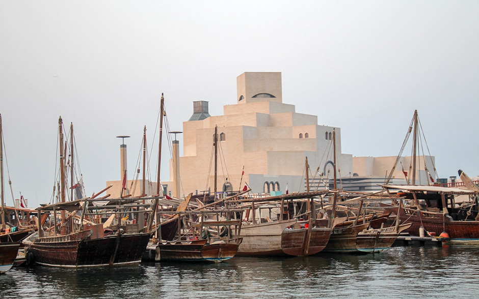 Traditional wooden dhows floating on the waters of Doha, Qatar, with the modern city skyline in the background at sunset.