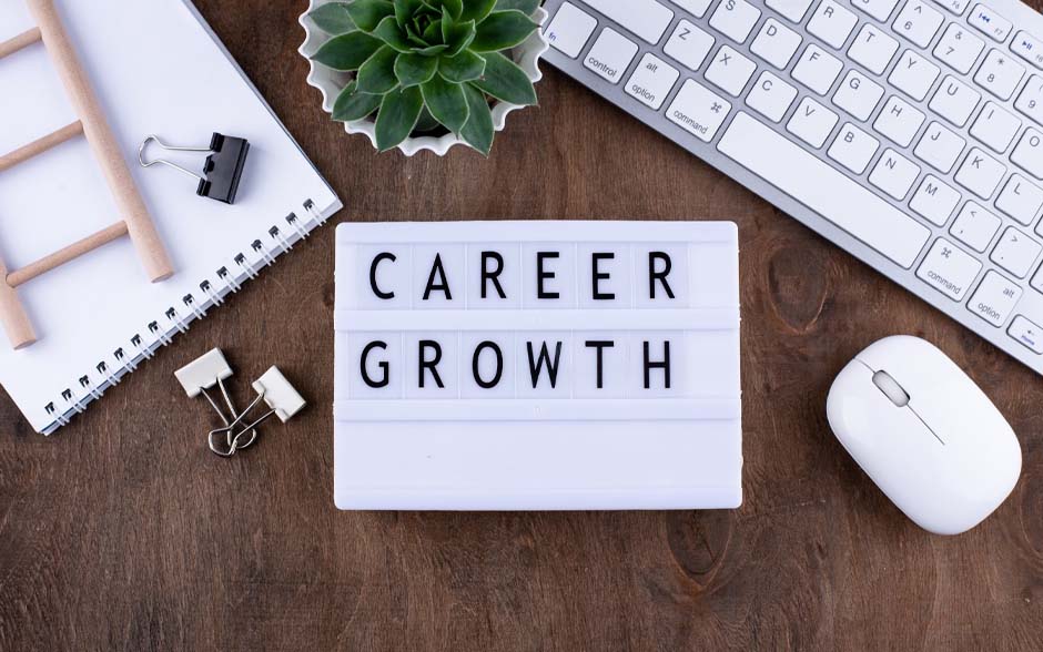 Photo of a white mouse, keyboard, blank notepad with a toy ladder, succulent, and a sign with "Career Growth" on it.