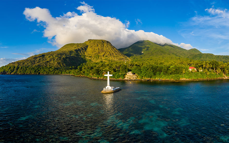 An aerial panorama of the Sunken Cemetery with a background of volcanos in the evening light on Camiguin Island.