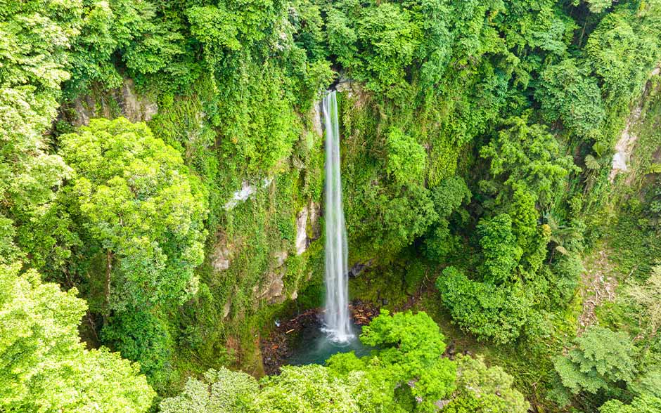 A waterfall in the middle of a mountain, surrounded by greenery.