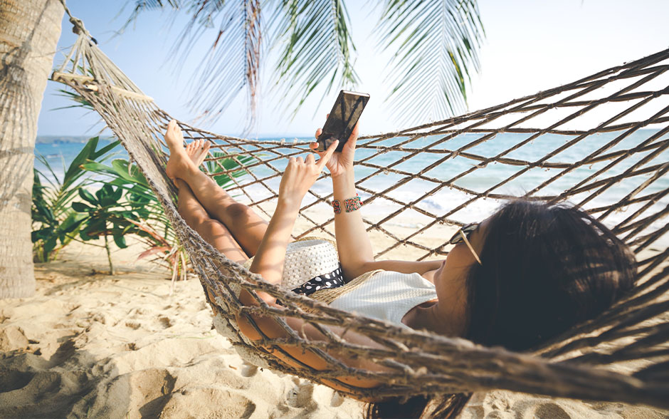 A young Asian woman using her mobile phone in a hammock.