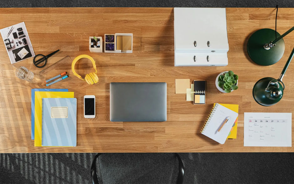Top view of a desk with laptop, smartphone, calendars, notebooks, and paperwork in home office.