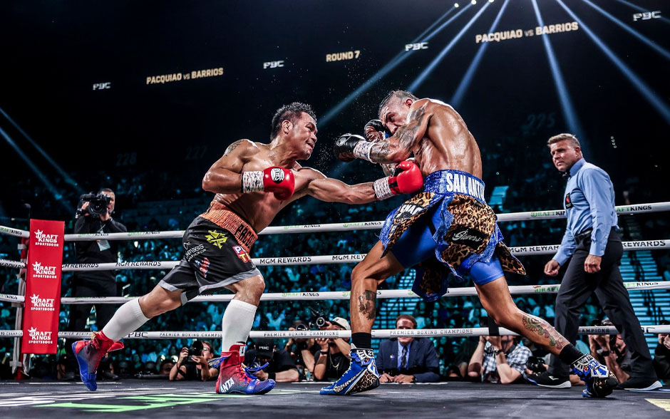 Two boxers, one in red-and-black and the other in blue-and-gold, fighting in a brightly lit ring.