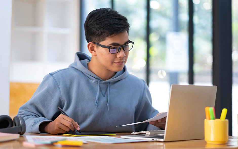 A young college student using a laptop, focused and multitasking.