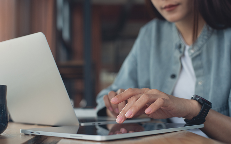 Woman using a digital tablet and working on a laptop computer on a wooden table.