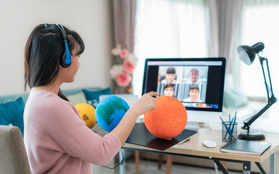 A woman participates in a video call on a desktop monitor showing four other people.