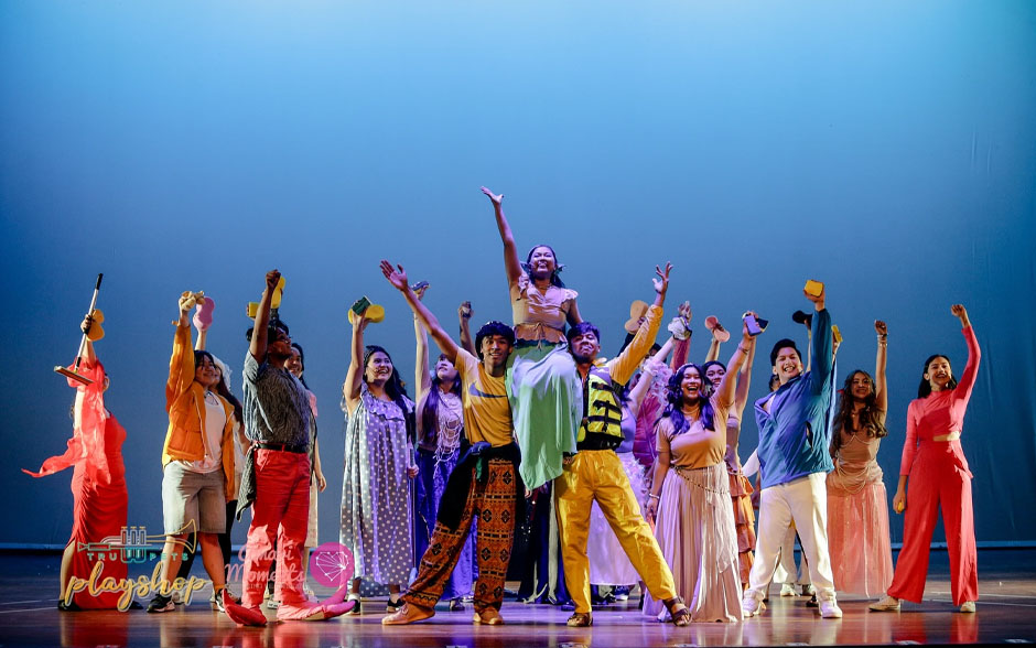 Kids and teens performing on stage in colorful costumes during a summer camp theater program.