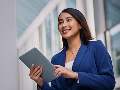 A smiling woman in a blue suit holding a tablet outside a building.