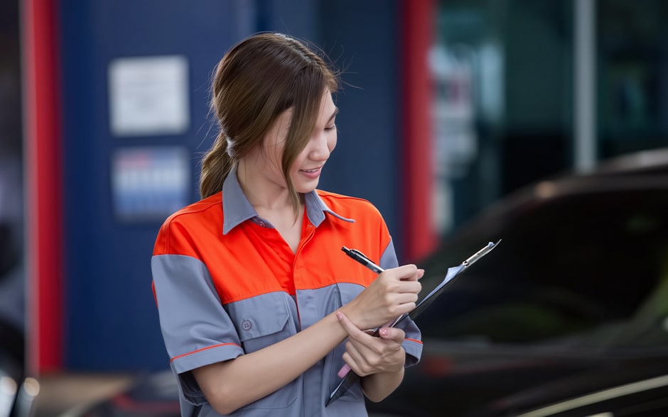 Young Asian woman writing in a clipboard after inspecting a car.