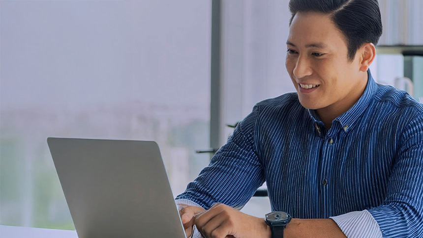 A professional man smiling while working on his laptop in an office.
