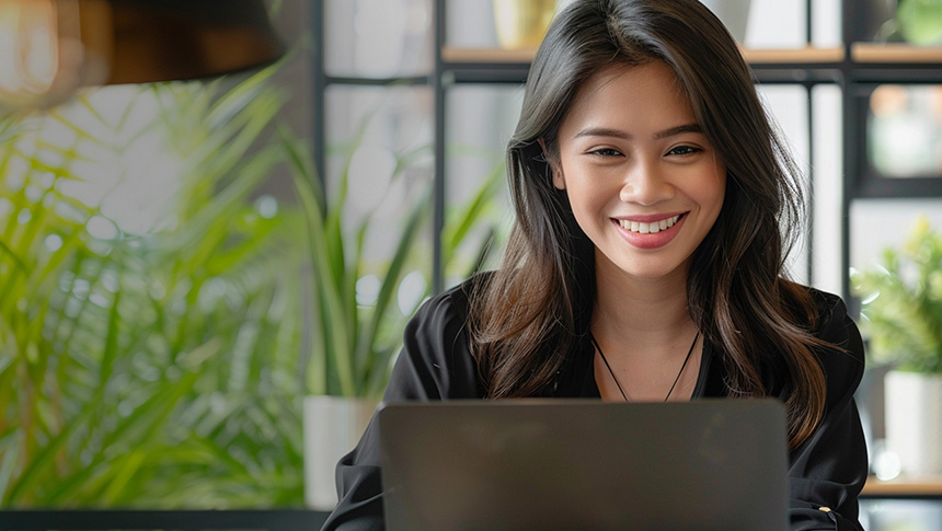 A woman smiling while working on her laptop in an office.