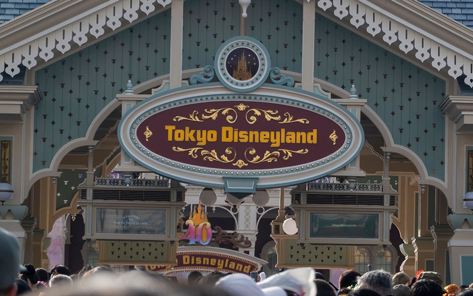 Entrance sign of Tokyo Disneyland with crowds of visitors gathered below