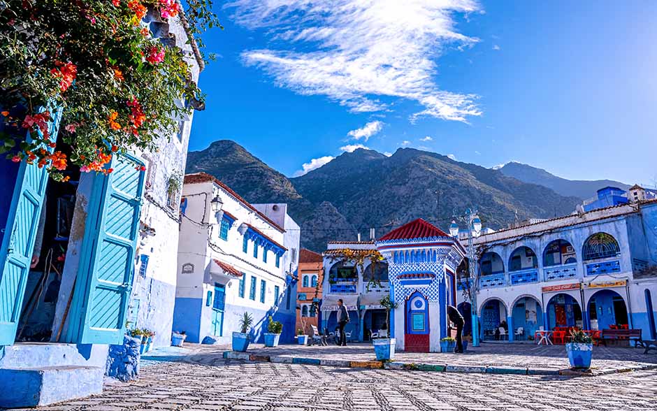 Blue-painted houses and a square in Chefchaouen, Morocco, with a mountain backdrop