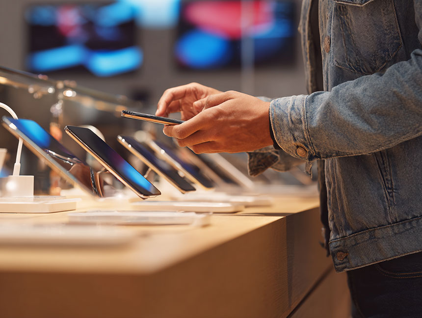 Customer testing smartphones at a store display, deciding between mobile options.