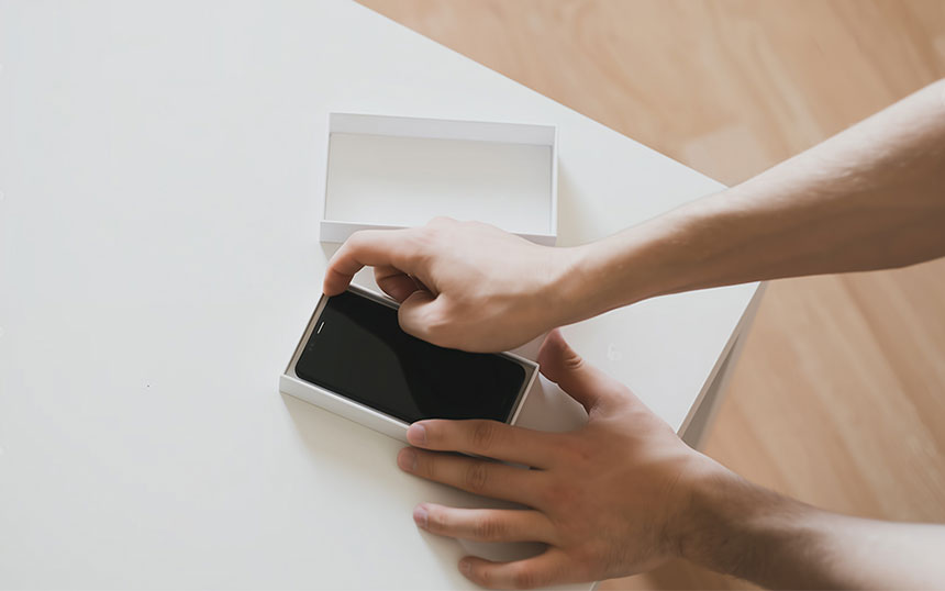 Photo of hands unboxing a new smartphone box on a white table.
