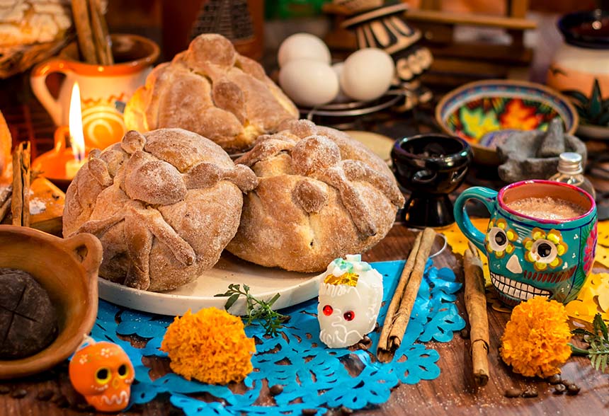 Close-up of traditional pan de muerto bread, sugar skulls, marigolds, and candles arranged on an altar