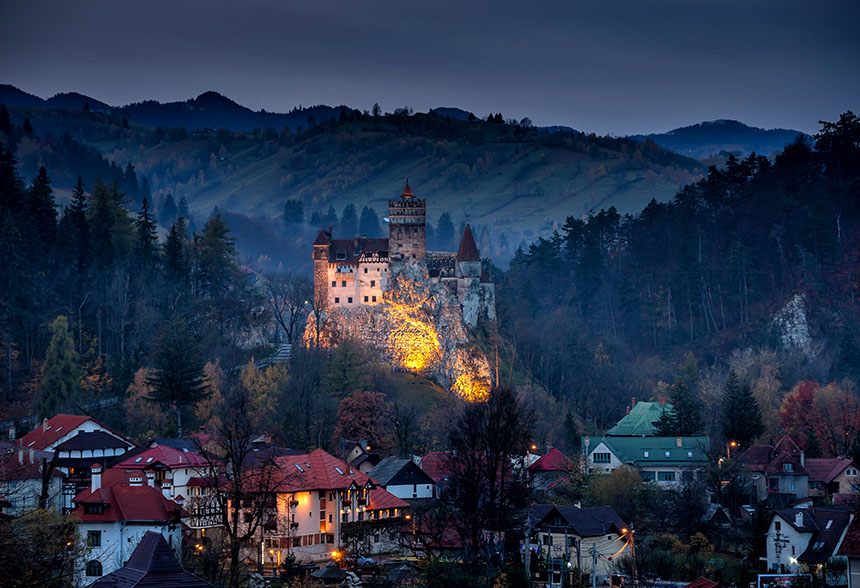 Twilight view of Bran Castle illuminated against the forested mountains.