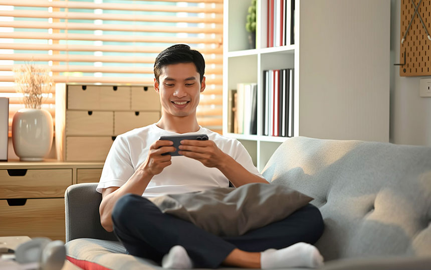 Smiling young Asian man using his smartphone on the sofa at home.