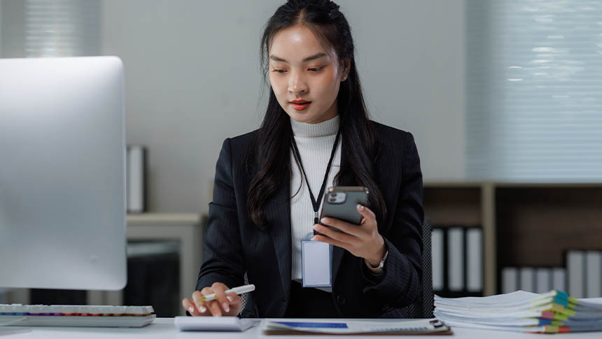 A female professional using her smartphone and a calculator for work.