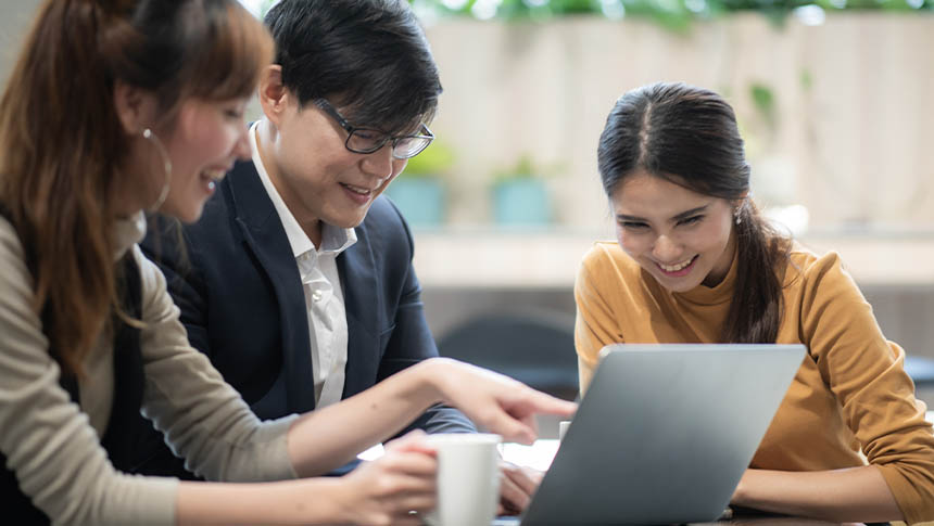 Three professionals checking the laptop at work while smiling and laughing.