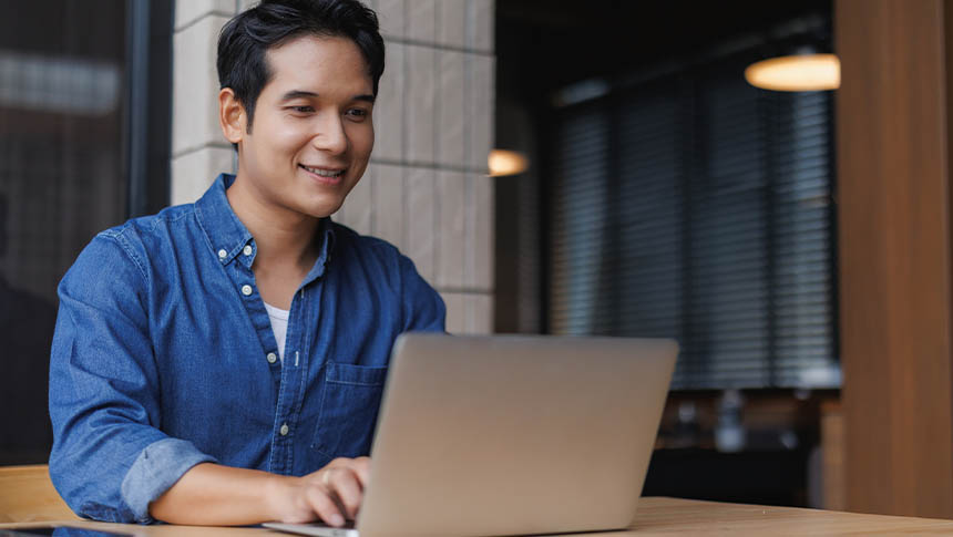 An Asian male using his laptop outside a cafe.