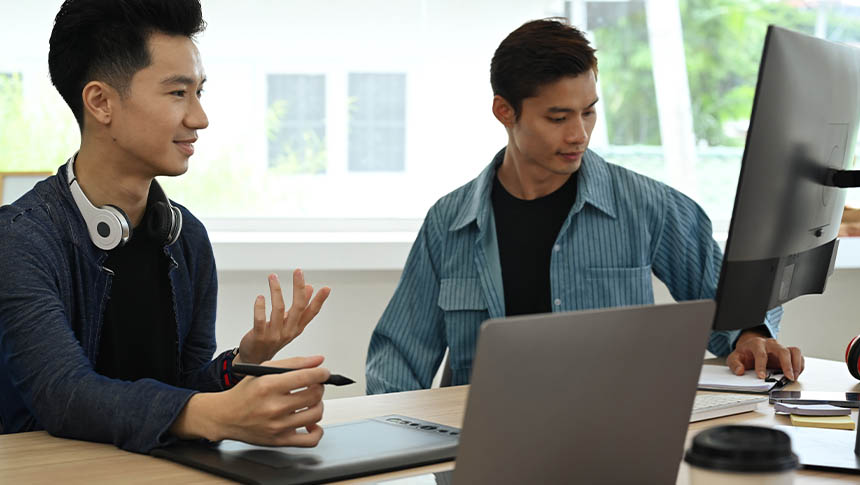 Two male professionals using a desktop computer for work.