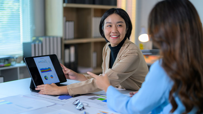 A female professional showing her colleague a chart on her tablet.