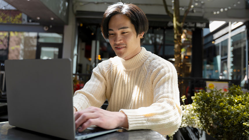 A male Asian working outside using his laptop.