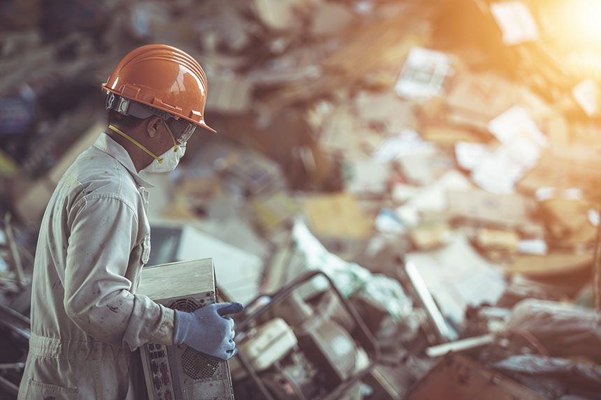 Worker in protective suits carries old CPU with e-waste behind him.