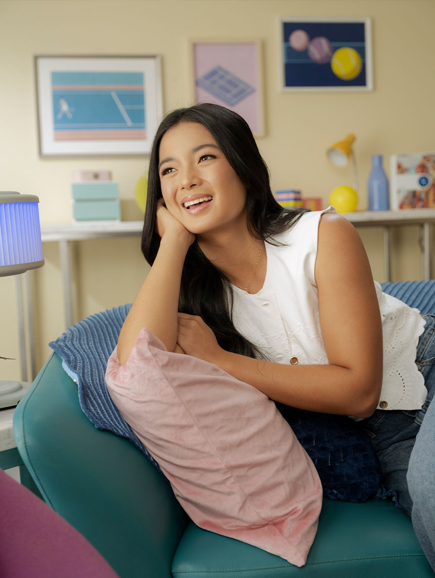 Alex Eala smiling while relaxing on a couch, resting her head on her hand.